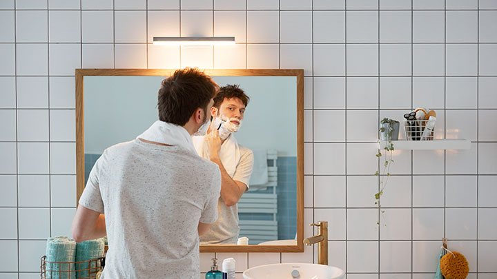 Hombre afeitándose delante de un espejo en el cuarto de baño iluminado con un LED de Philips de montaje en pared
