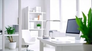 Una habitación blanca y luminosa muestra un escritorio con un ordenador y una lámpara de mesa sobre él